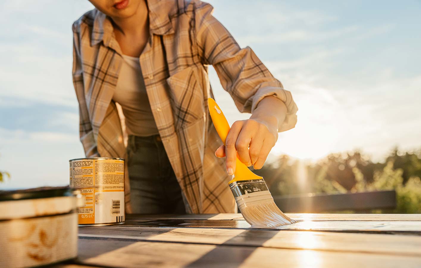 Eine junge Frau streicht einen Tisch bei strahlendem Sonnenschein